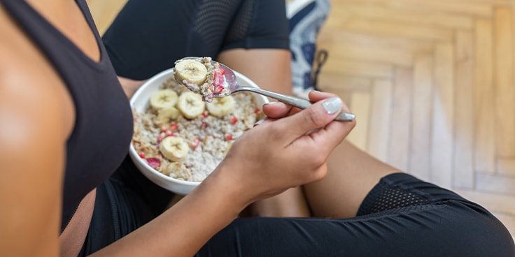 Schotel met havermout, bananen en bessen in de handen van een vrouw in sportkleding.