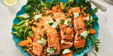 Gerecht met gegrilde zalm, kikkererwten, wortels en groene bladgroenten op een blauwe schaal.