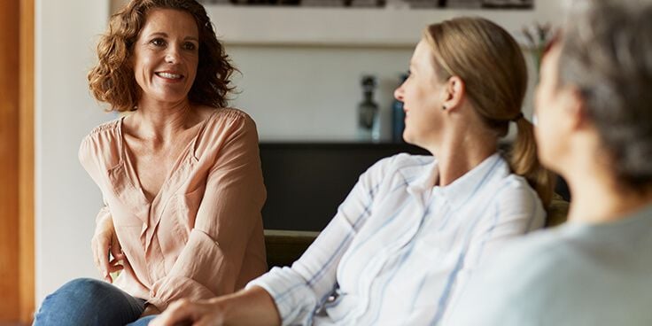 Drie vrouwen in gesprek in een comfortabele woonkameromgeving.