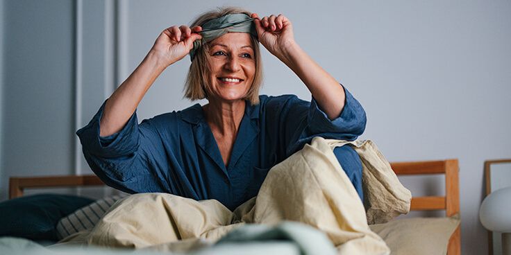 Persoon in pyjama die een slaapmasker vastmaakt in bed