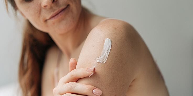 Vrouw die lotion aanbrengt op haar schouder.