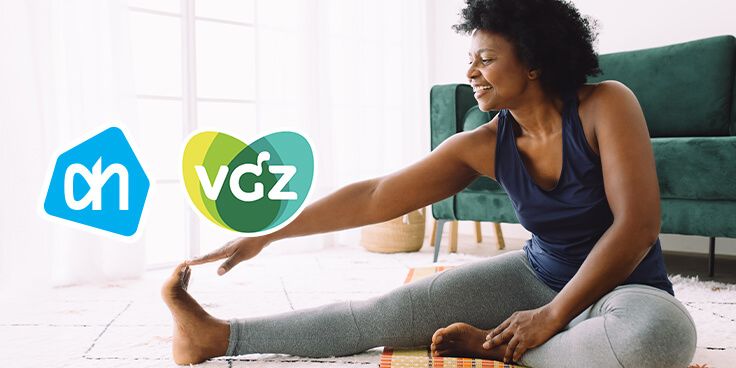 Vrouw doet een stretch oefening in de woonkamer met Albert Heijn en VGZ logo's op de voorgrond.