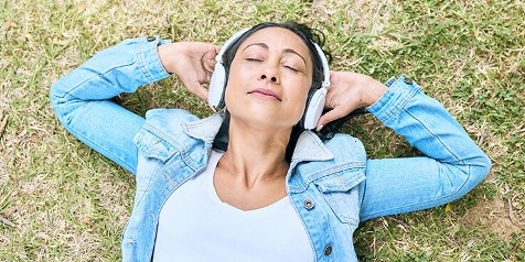 Persoon in een spijkerjasje liggend op gras met een koptelefoon op