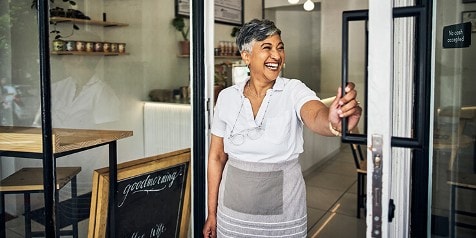 Vrouw in een schort opent de deur van een café of winkel.