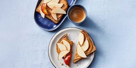 Gebakken boterham met pindakaas en plakjes appel, geserveerd met een kopje koffie.