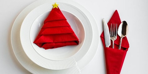 Servet gevouwen als kerstboom op een wit bord naast bestek in een rode servet.