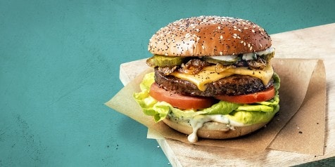 Hamburger met kaas, tomaat, sla, augurk en gekarameliseerde uien op een maanzaadbroodje.