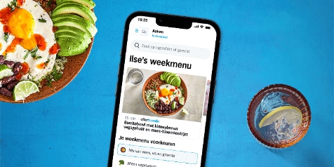 Smartphone die Ilse's weekmenu laat zien met een gerecht van burritobowl met kidneybonen, vegagehakt en munt-bloemkoolrijst naast een glas water met een schijfje citroen en een bord saladaankleding.