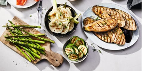 Gegrilde groenten op een tafel met asperges, tomaten, paprika, venkel, courgette, maïs en aubergine.