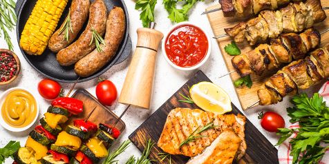 Gegrilde gerechten met worstjes, maïskolf, groentespiesjes, kipfilet en vleesspiesjes, geserveerd met saus en kruiden.