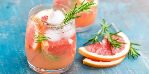 Verfrissende grapefruitcocktail met ijs en rozemarijn, geserveerd op een blauwe tafel.
