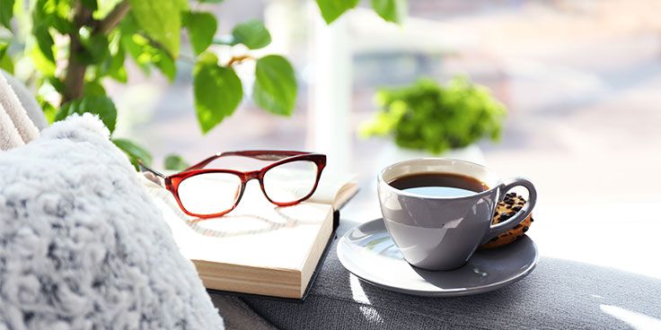 Bril, boek en een kop koffie op een gezellige bank bij het raam