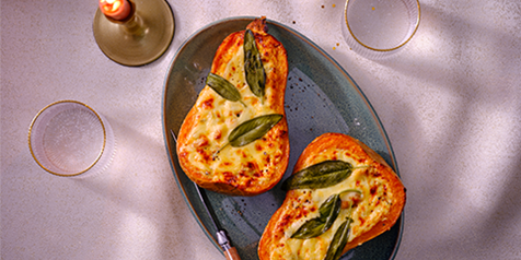 Geroosterde pompoenhelften gevuld met gesmolten kaas en verse saliebladeren op een schaal.