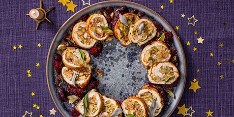 Kerstfeestelijke maaltijdopstelling met gevulde kalkoenrolletjes op een bord, versierd met rode vruchten en sterren op een paarse tafelkleed.