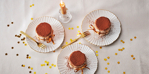 Drie tiramisu's op witte borden, omringd door gouden sterrenconfetti en een brandende kaars.