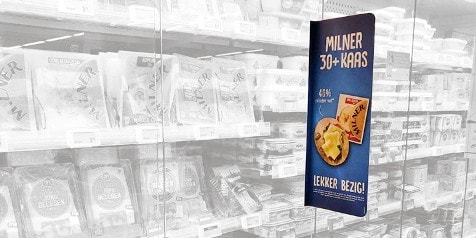 Reclamebord voor Milner 30+ kaas met een afbeelding van het product, waaronder de tekst "40% minder vet" en "Lekker bezig!". In de achtergrond is een koelvak met andere kaasproducten zichtbaar.