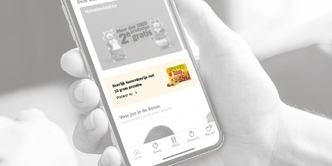 Iemand houdt een smartphone vast met een afbeelding op het scherm van een productpromotie. De promotie betreft ontbijtgranen van het merk Quaker met de tekst "Heerlijk lussendoortje met 10 gram proteïne".
