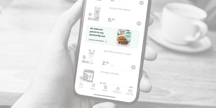 Smartphone met Albert Heijn app geopend met productaanbod, inclusief Alpro Mild & Creamy en YVIA plantaardige yoghurt.