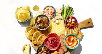 Borrelplank met verschillende hapjes zoals chips, garnalen, vleeswaren, kaas, groentesticks, crackers, bruschetta, olijven, dips en noten.