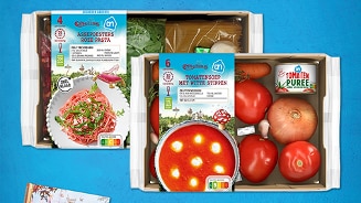 AH maaltijdpakketten voor aspergesters roze pasta en tomatensoep met witte stippen, samen met het boek 'Efteling sprookjes bakboek' op een blauwe achtergrond. Tekst: "Reageer en maak kans!"