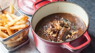 Stoverij in een rode kookpan met een bijgerecht van friet in een metalen mandje.