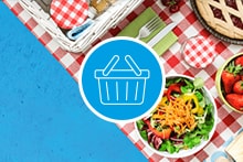 Picknick op een rood-wit geruite deken met een mand vol fruit, groenten en broodjes.