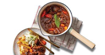 Stoofpot met groenten in een pan op een handdoek naast een bord met frietjes en rauwkostsalade.