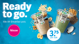 Twee AH Breakfast pots, één met oats banaan en brood, en één met chia pandan en kokos, gepresenteerd op een blauwe achtergrond met ontbijtgranen, bananen- en kokosstukjes. Promotietekst: "Ready to go", prijs €3,75 per stuk, en label "Nieuw".