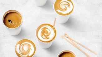 Kopjes koffie met melkschuim en roerstaafjes op een lichte achtergrond, ideaal voor onderweg.