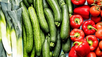Verse prei, komkommers, rode paprika's en tomaten op een lichtblauwe achtergrond.
