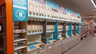 Zelfbedieningsstation bij Albert Heijn met dispensers voor ontbijtgranen, zaden, pitten en noten, met een duurzame verpakkingsoptie.