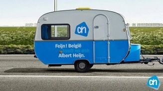 Caravan met Albert Heijn-logo en tekst "Feijn! België heeft nu ook Albert Heijn" langs de weg.