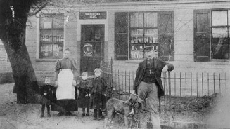 Historische foto van een gezin voor een winkel met een hond, met "Van Houten's cacao" op het raam.