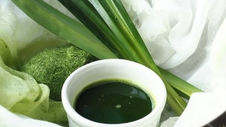 Groene sap in een witte kom met verse pandanbladeren en gemalen pandan.