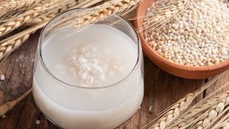 Glas haverdrank met haverkorrels en gedroogde halmen op houten ondergrond.