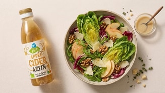 Fles AH Biologisch appelciderazijn naast een salade met appel, walnoten, Parmezaanse kaas, sla en dressing.
