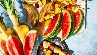 Schijven watermeloen, ananas, meloen en fruitspiesen met druiven en stukjes ananas en mango op een lichte ondergrond.