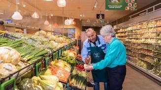 Twee klanten in de Albert Heijn groente- en fruitafdeling, omringd door verse groenten.