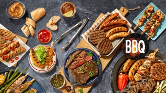 Diverse selectie van gegrild vlees, hamburgers, worsten, spiesjes en groente op een tafel, met brood en sauzen, gepresenteerd voor een BBQ.