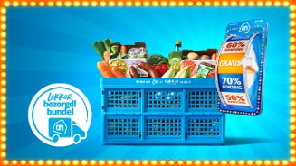 Blauwe Albert Heijn bezorgkrat gevuld met diverse boodschappen en verse groenten, naast een kaart met kortingen tot 70% en de tekst "lekker bezorgd! bundel" op een blauwe achtergrond met lichteffecten.