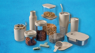 Set van bewaardozen, voorraadpotten, koffiebekers, bakjes en clips op een blauwe achtergrond, gevuld met onder andere koekjes, koffiebonen, granola en zaden.