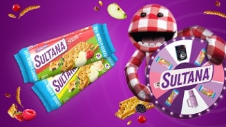 Afbeelding van Sultana fruitkoekjes verpakkingen en een vrolijk rood-wit geblokt poppetje dat een prijzenrad vasthoudt op een paarse achtergrond met verspreide vruchten en graan.