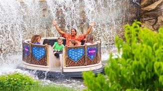 Groep mensen in een ronde boot die een wildwaterbaan beleeft bij een waterval, omgeven door groen.