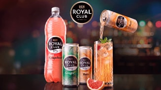 Flessen en blikjes Royal Club frisdrank, waaronder Pink Grapefruit, Ginger Ale en Ginger Beer, naast een glas gevuld met ijsklontjes, verse munt en een partje grapefruit. Een blikje wordt leeggeschonken in het glas. Op de achtergrond is het Royal Club logo zichtbaar.