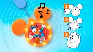 Donald Duck hanger in de vorm van Mickey Mouse, met lichtjes en muzieknoten, op een blauwe achtergrond. Rechts instructietekening in drie stappen voor het bevestigen van de hanger aan een rugzak.