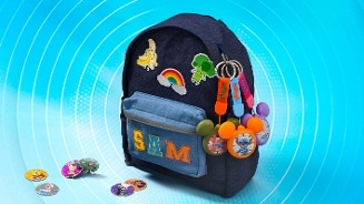 Donkerblauwe rugzak met de naam "SAM" op het voorvak, versierd met vrolijke patches zoals een banaan, broccoli en een regenboog. Aan de rits hangen sleutelhangers met figuren. Voor de rugzak liggen verschillende gekleurde schijfjes met illustraties. Achtergrond met blauwe cirkelpatronen.