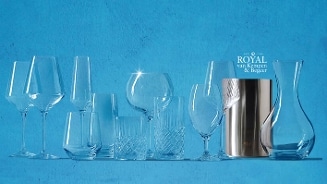 Verschillende glazen en een karaf uit de collectie van Royal van Kempen & Begeer tegen een blauwe achtergrond