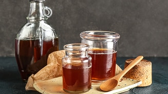 Fles en potten met honingkleurige siroop en houten lepel op een bord