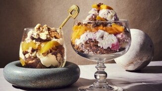 Twee stijlvolle glazen gevuld met desserts, versierd met verschillende lagen room, fruit en koekjesstukken.