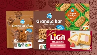 Verschillende ontbijt- en snackproducten van Albert Heijn en Liga, waaronder AH Granola bites Choco almond, AH Granola bar Chocolade, AH Dieren koekjes, en Liga Milkbreak melk-aardbeiensmaak, gepresenteerd tegen een decoratieve achtergrond met koekjespatroon.